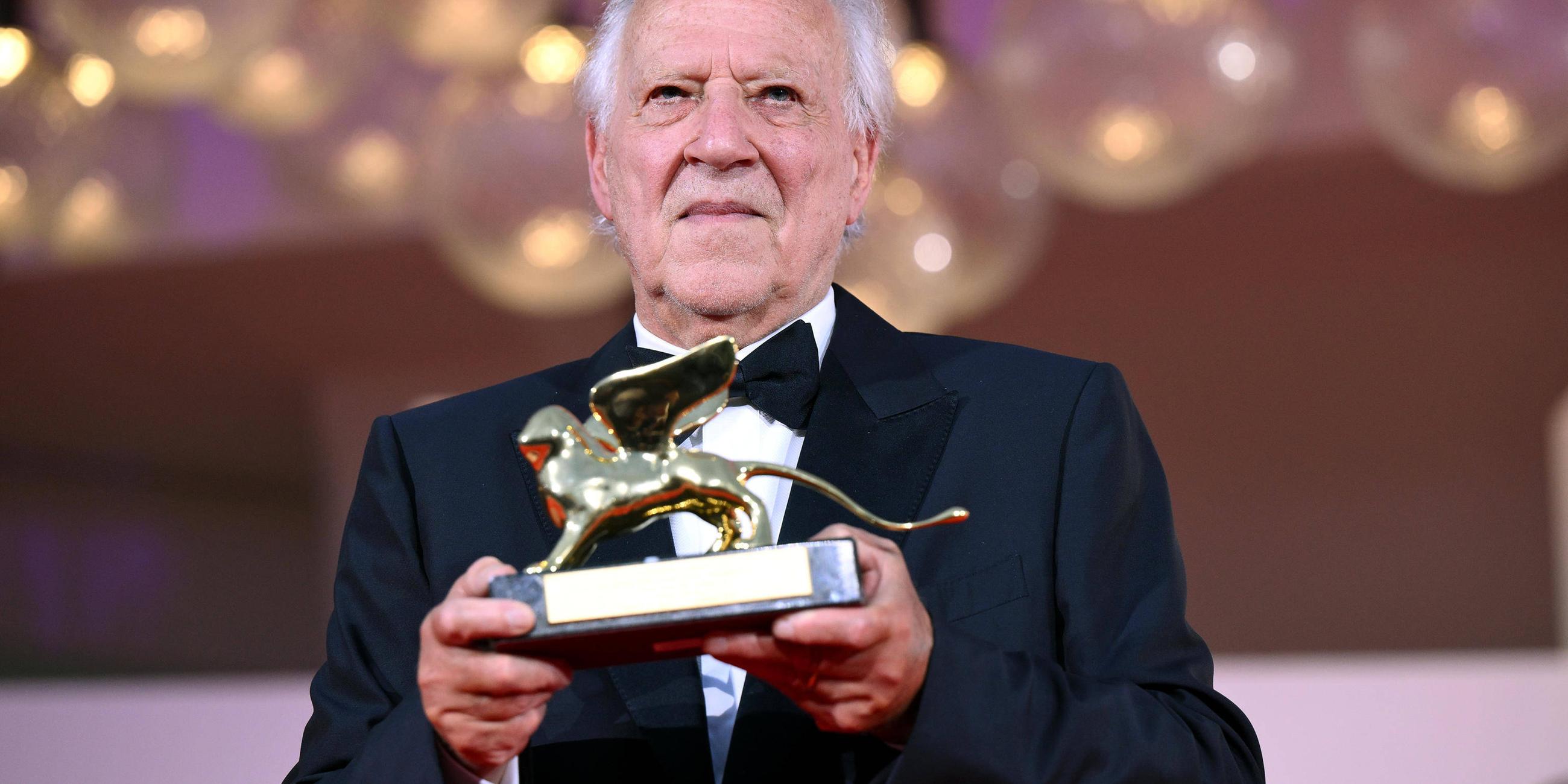 Werner Herzog hält einen Ehrenpreis der Filmfestspiele in der Hand.