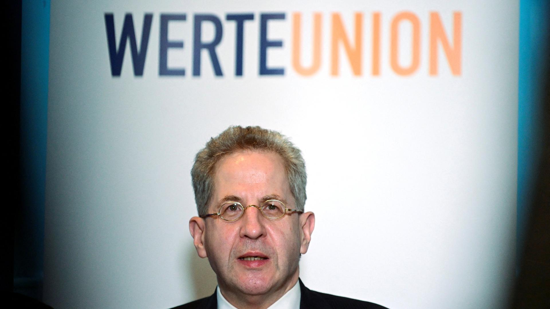 Hans-Georg Maaßen steht vor einem Plakat mit der Aufschrift "Werteunion".