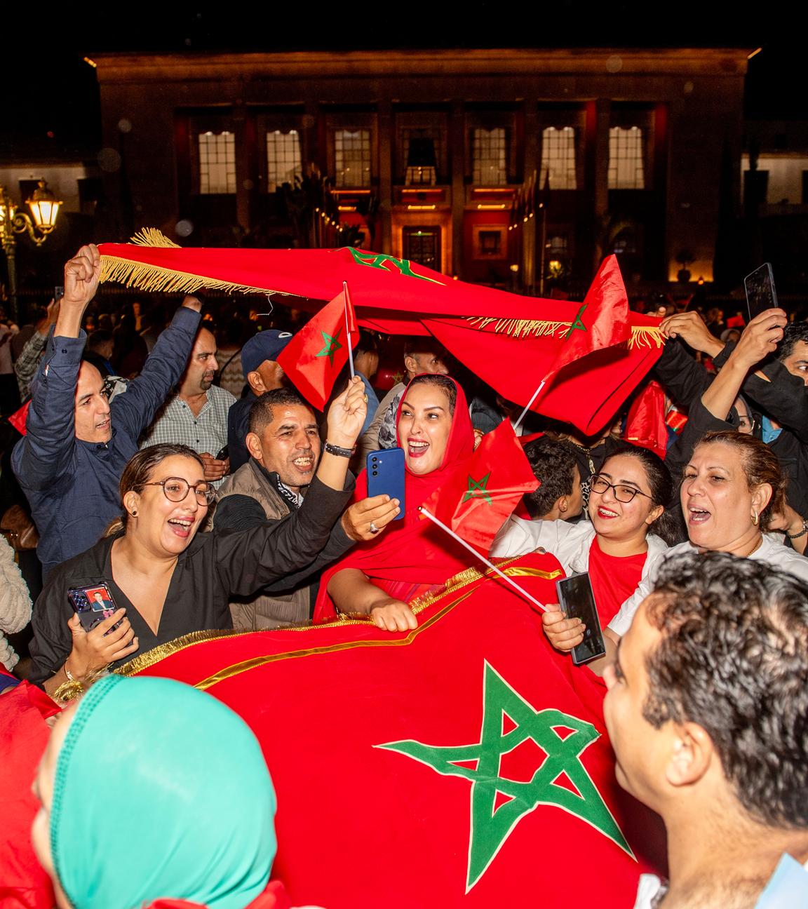Menschen stehen gemeinsam auf der Straße und jubeln. Sie halten Marrokko-Fahnen hoch