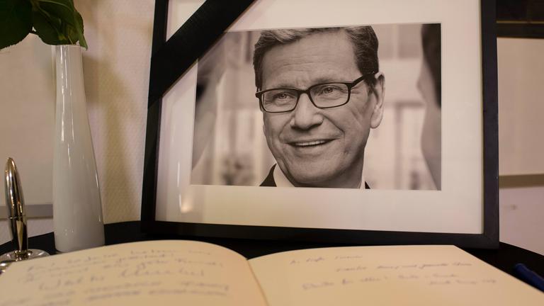 ein foto von guido westerwelle steht am 18.03.2016 auf einem tisch neben einem kondolenzbuch im eingangsbereich des thomas-dehler-haus in berlin. der ehemalige aussenminister war am 18.03.2016 an den folgen seiner leukaemie-erkrankung gestorben.