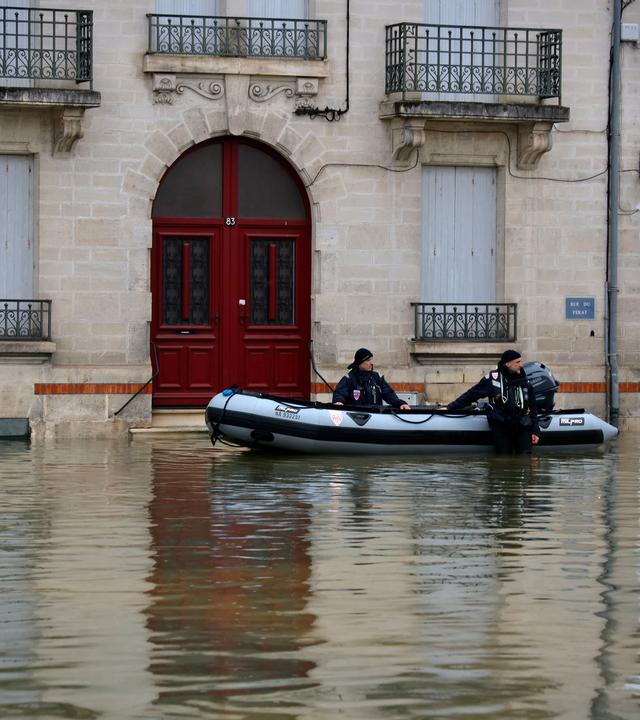 18.02.2026, Frankreich, Saintes: Polizeibeamte stehen in einer überfluteten Straße in Saintes, als schwere Überschwemmungen den Westen Frankreichs inmitten des Sturms Pedro treffen.