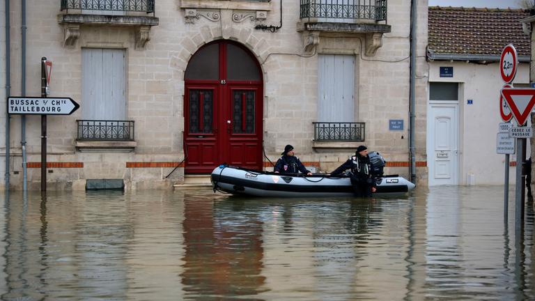18.02.2026, Frankreich, Saintes: Polizeibeamte stehen in einer überfluteten Straße in Saintes, als schwere Überschwemmungen den Westen Frankreichs inmitten des Sturms Pedro treffen.