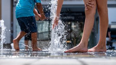 Kinder erfrischen sich bei sommerlichen Temperaturen an einem Brunnen am Theresienplatz. 