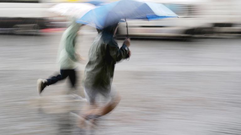 Passanten laufen bei starkem Regen über den Odeonsplatz in der bayerischen Landeshauptstadt.