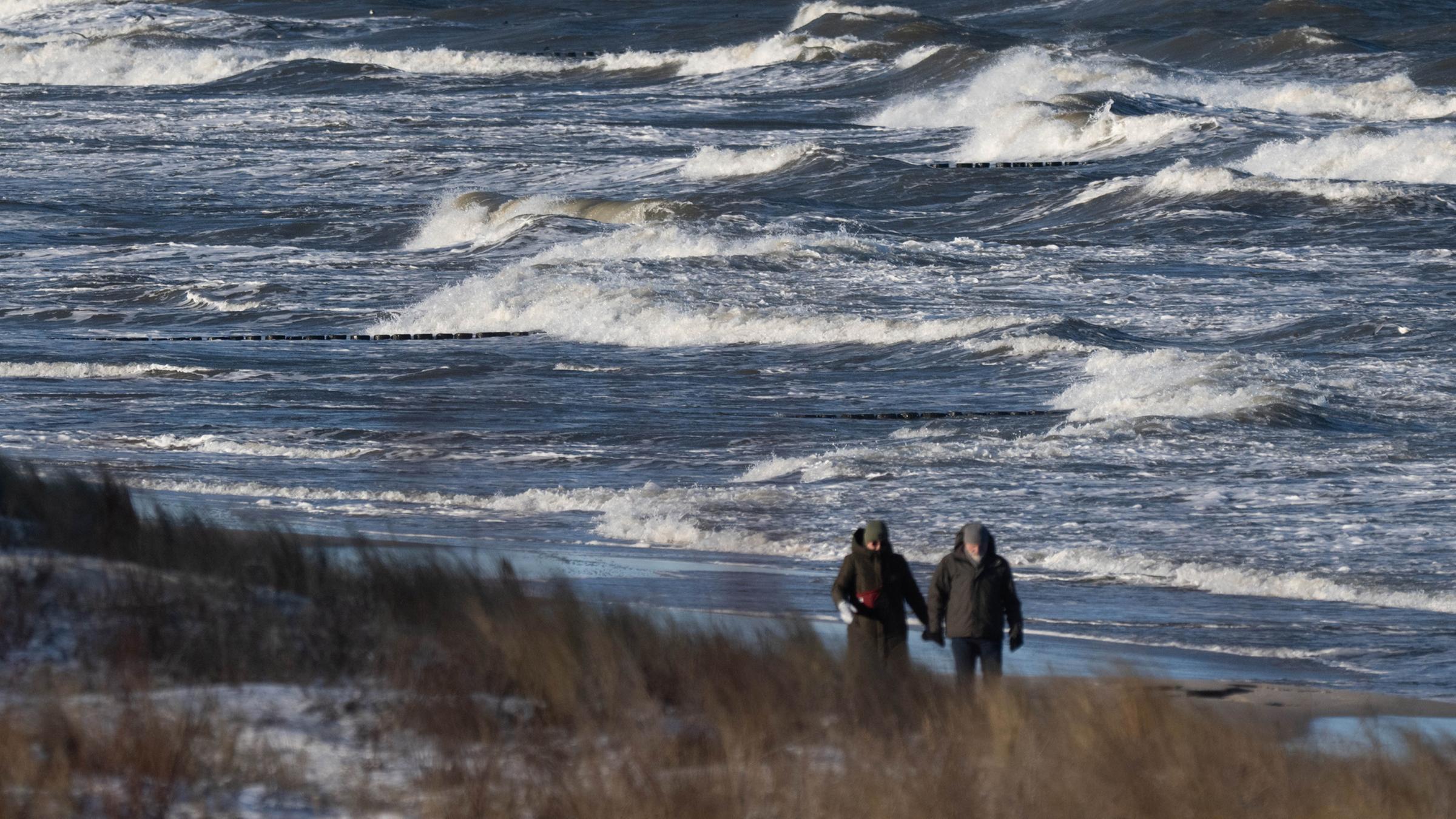 Menschen laufen am 11.01.2026 im Seebad Koserow am Strand entlang.