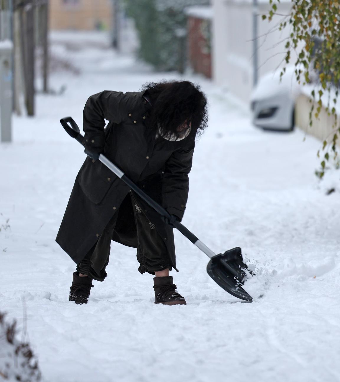 Mecklenburg-Vorpommern, Rostock: Eine Frau ist mit Schneeschieber in Aktion in einer eingeschneiten Straße.