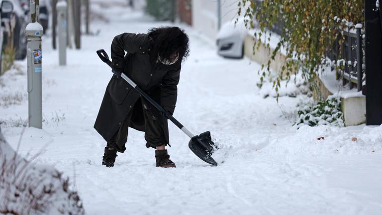 Mecklenburg-Vorpommern, Rostock: Eine Frau ist mit Schneeschieber in Aktion in einer eingeschneiten Straße.