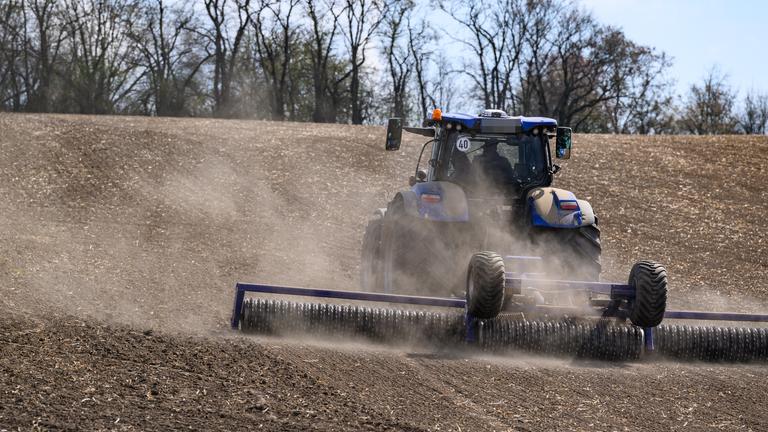 Brandenburg, Podelzig: Ein Landwirt glättet den trockenen Ackerboden mit einer speziellen Walze und wirbelt dabei viel Staub auf.