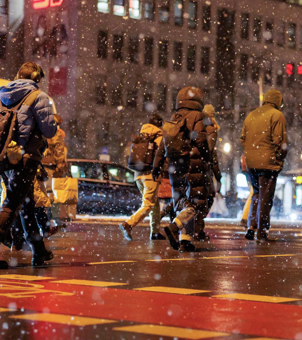 Fußgänger überqueren die Straße am Wiesbadener Hauptbahnhof im Schneetreiben.