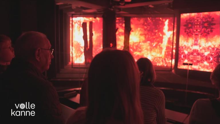 Besucher in der Ausstellung "Wetterextreme" vor einem brennenden Bereich