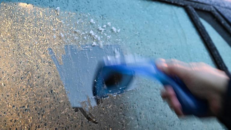 18.11.2025, Baden-Württemberg, Stuttgart: Ein Mann kratzt am Morgen eine Autoscheibe von einer Eisschicht frei.