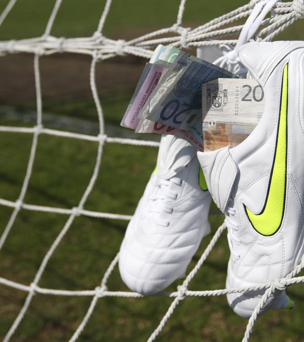 Wettskandal im Fussball. Nike Fussballschuhe gefüllt mit Geldscheinen hängen am Tornetz