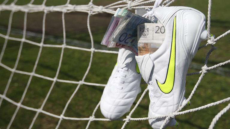 Wettskandal im Fussball. Nike Fussballschuhe gefüllt mit Geldscheinen hängen am Tornetz