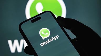 Hand hält Smartphone, auf dem Bildschirm ist groß das WhatsApp-Logo zu sehen.