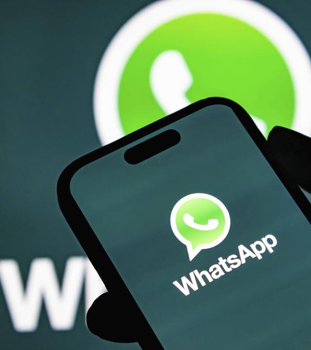 Hand hält Smartphone, auf dem Bildschirm ist groß das WhatsApp-Logo zu sehen.