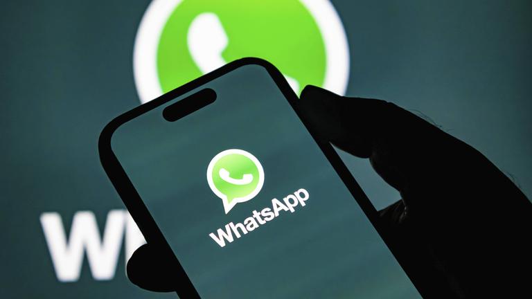 Hand hält Smartphone, auf dem Bildschirm ist groß das WhatsApp-Logo zu sehen.