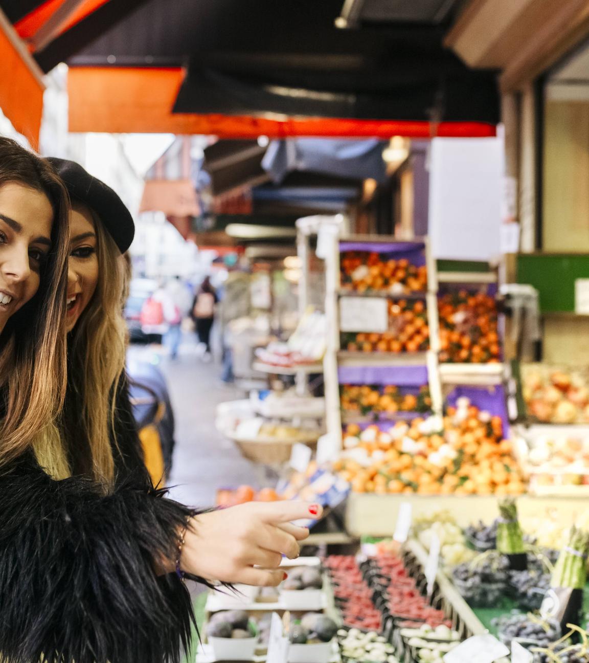 Zwei Frauen stehen vor einem Obst- und Gemüsestand 