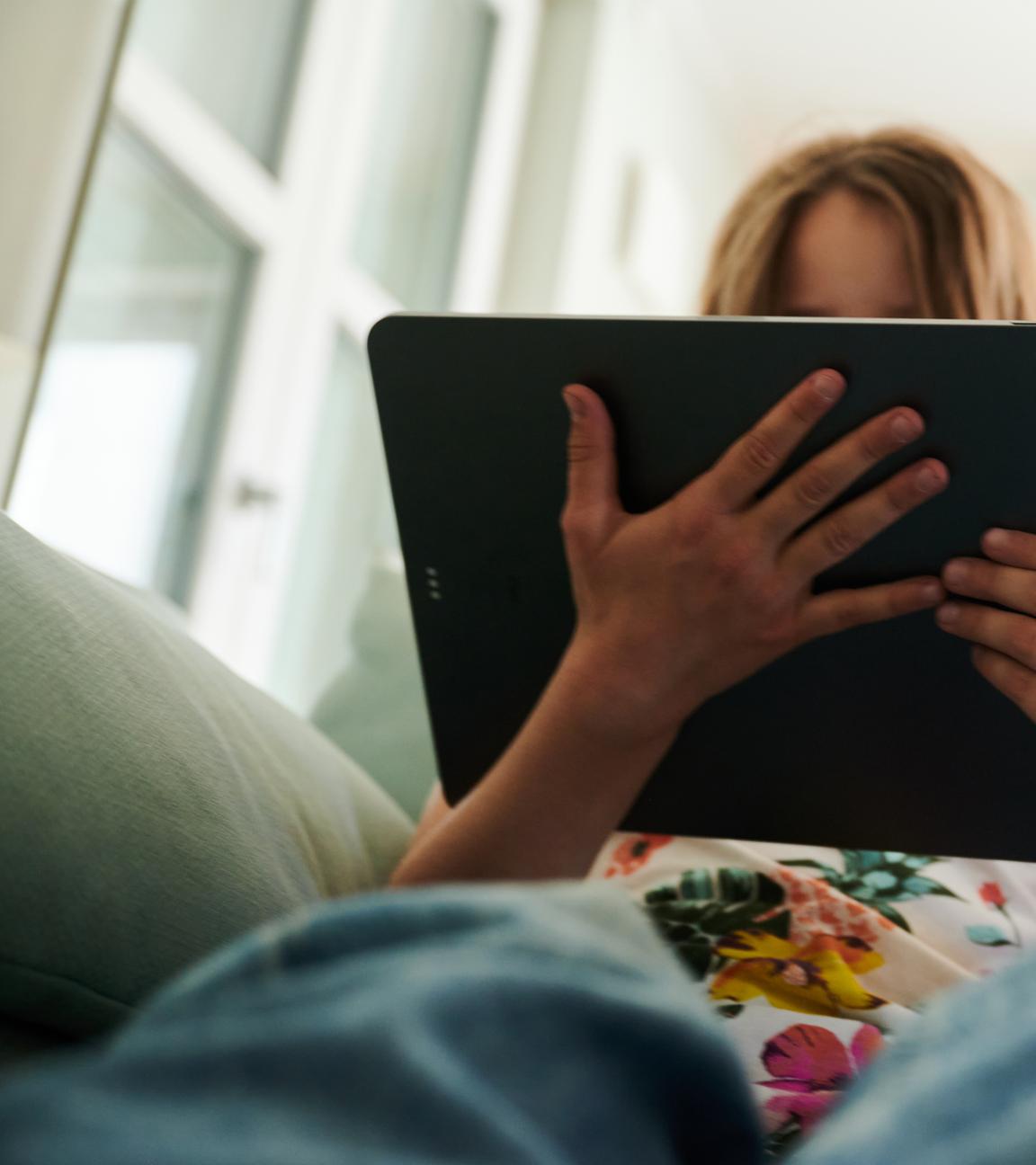 Symbolbild: Ein Mädchen sitzt auf der Couch und guckt auf ein Tablet