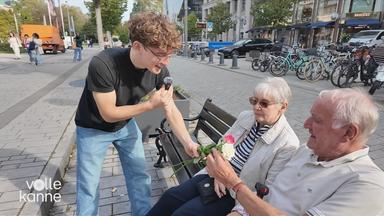 Ein Reporter überreicht einem älteren Ehepaar eine Rose.