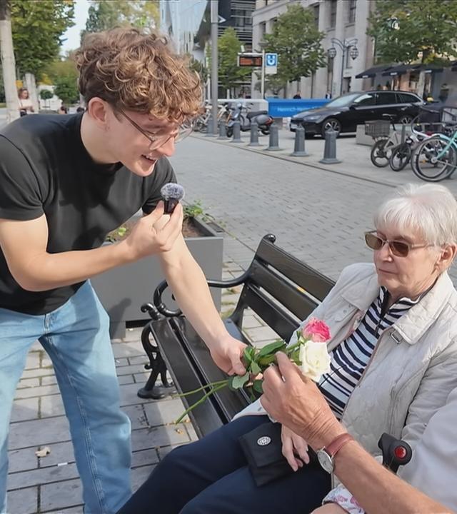 Ein Reporter überreicht einem älteren Ehepaar eine Rose.