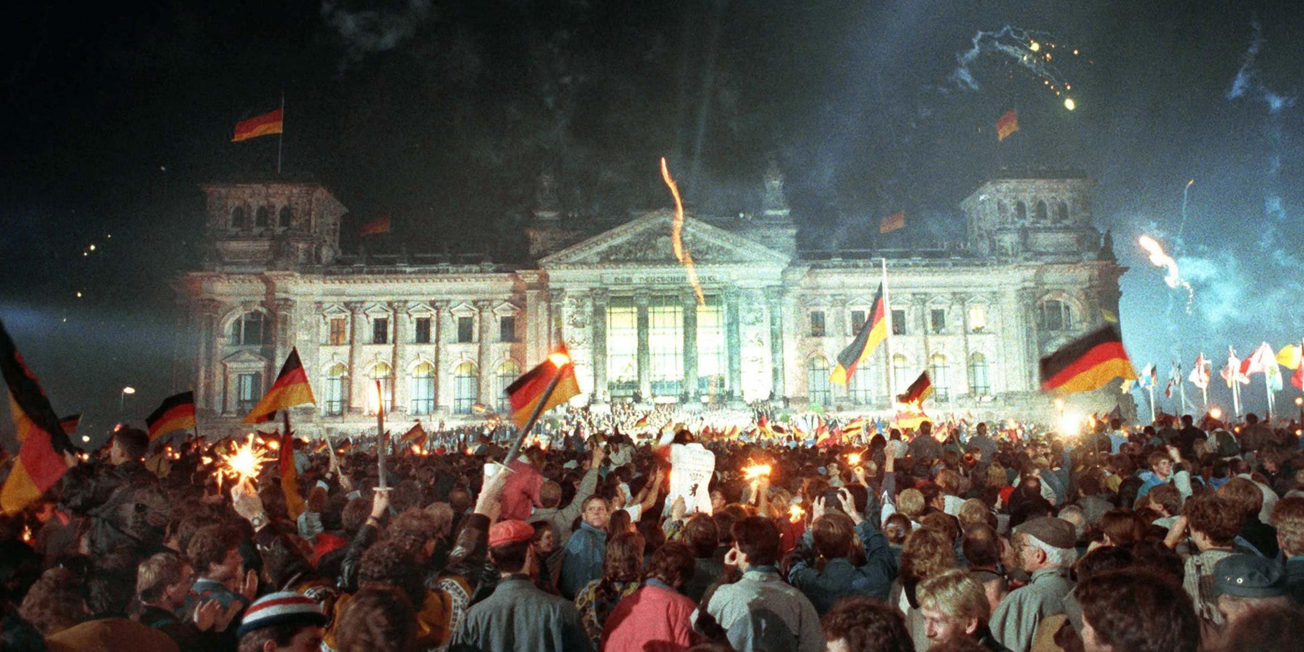 Am 3. Oktober 1990 feiern jubelnde Menschen vor dem Berliner Reichstag mit Feuerwerk, Deutschlandfahnen und Volksfeststimmung die wiedergewonnene Einheit Deutschlands.