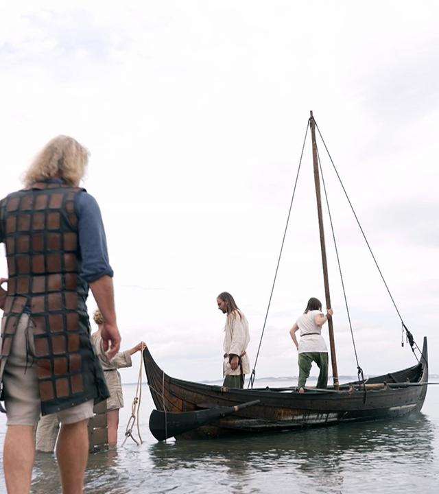Menschen verkleidet als Wikinger stehen auf einem Boot ud am Strand