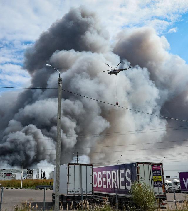Ein Löschhelikopter fliegt nach einem ukrainischen Drohnenangriff über der qualmenden Wildberries-Filiale.