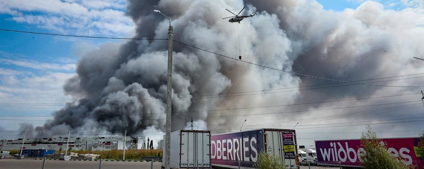 Ein Löschhelikopter fliegt nach einem ukrainischen Drohnenangriff über der qualmenden Wildberries-Filiale.