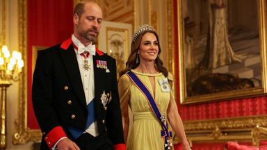 William und Kate betreten einen Raum in feierlicher Garderobe. 