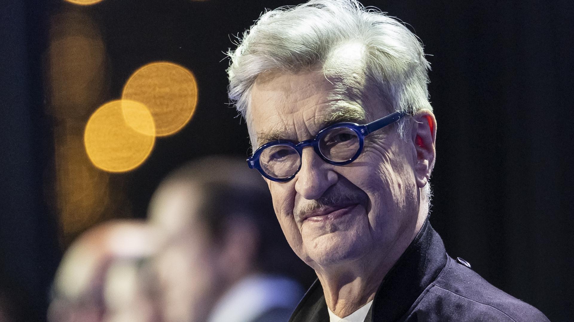 Wim Wenders, deutscher Regisseur, schaut in die Kamera. Er trägt eine runde dunkelblaue Brille.