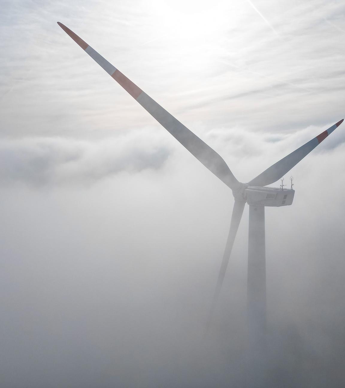 Die Windräder in einem Windpark westlich von Halle ragen aus dem Morgennebel hervor.