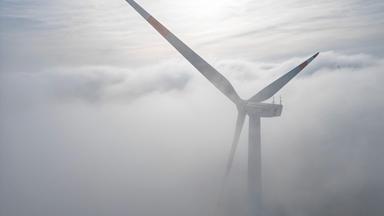 Die Windräder in einem Windpark westlich von Halle ragen aus dem Morgennebel hervor.