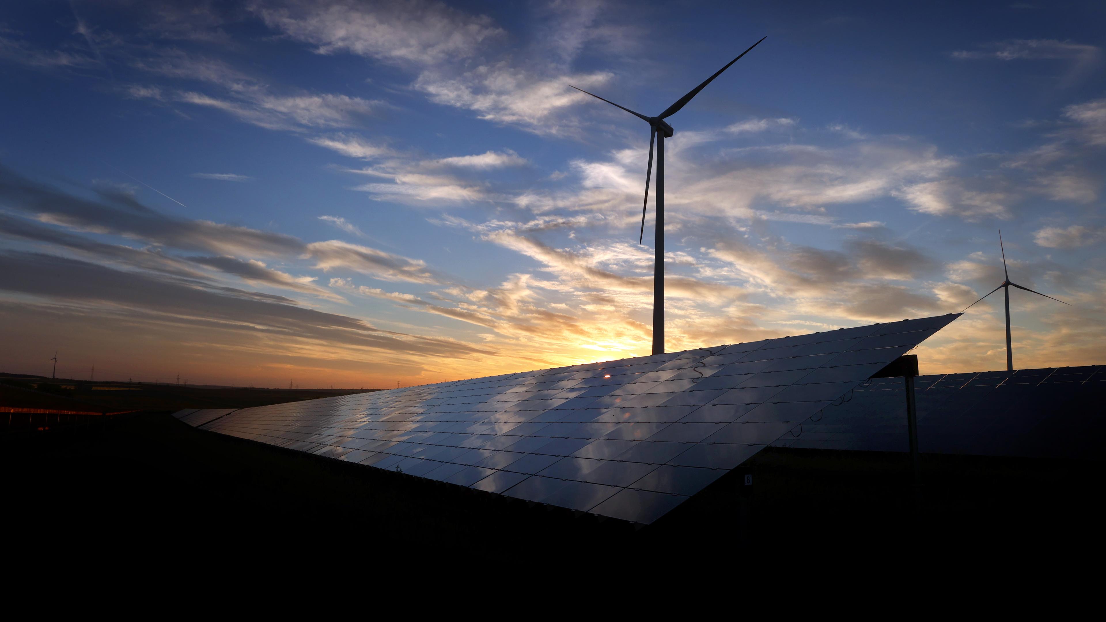 Ein Windkraftanlage und im Vordergrund ein Solarpark bei Sonnenuntergang 