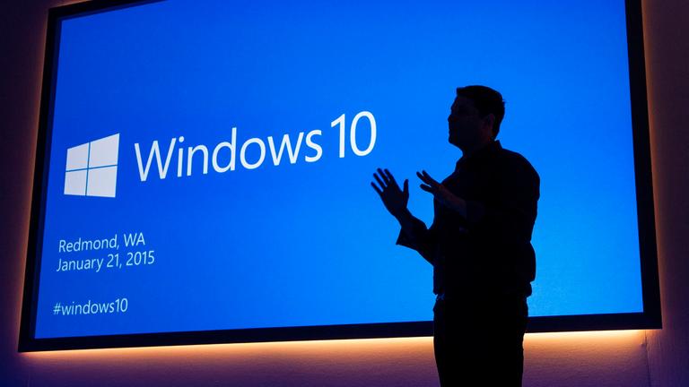 Microsoft Executive Vice President Terry Myerson beid er Präsentation von Windows 10 im Januar 2015. Man sieht nur seine Umrisse vor der blauen Präsentationsfolie.