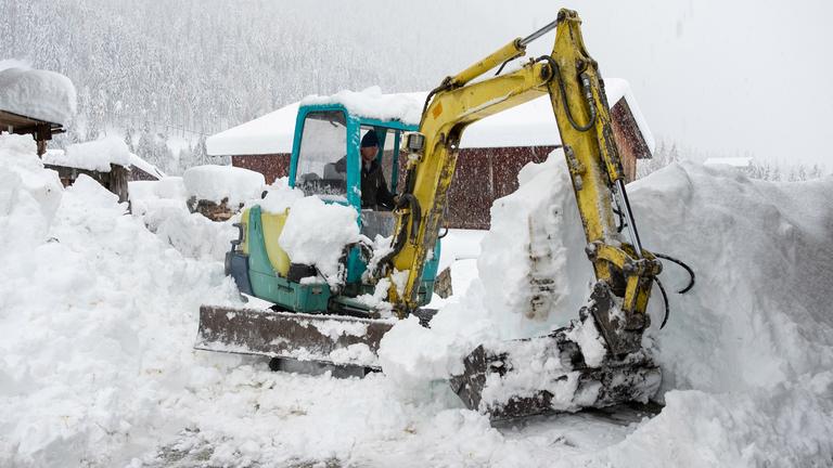 Ein Mann in einem Bagger ist mit der Schneeräumung in Kals am Grossglockner beschäftigt