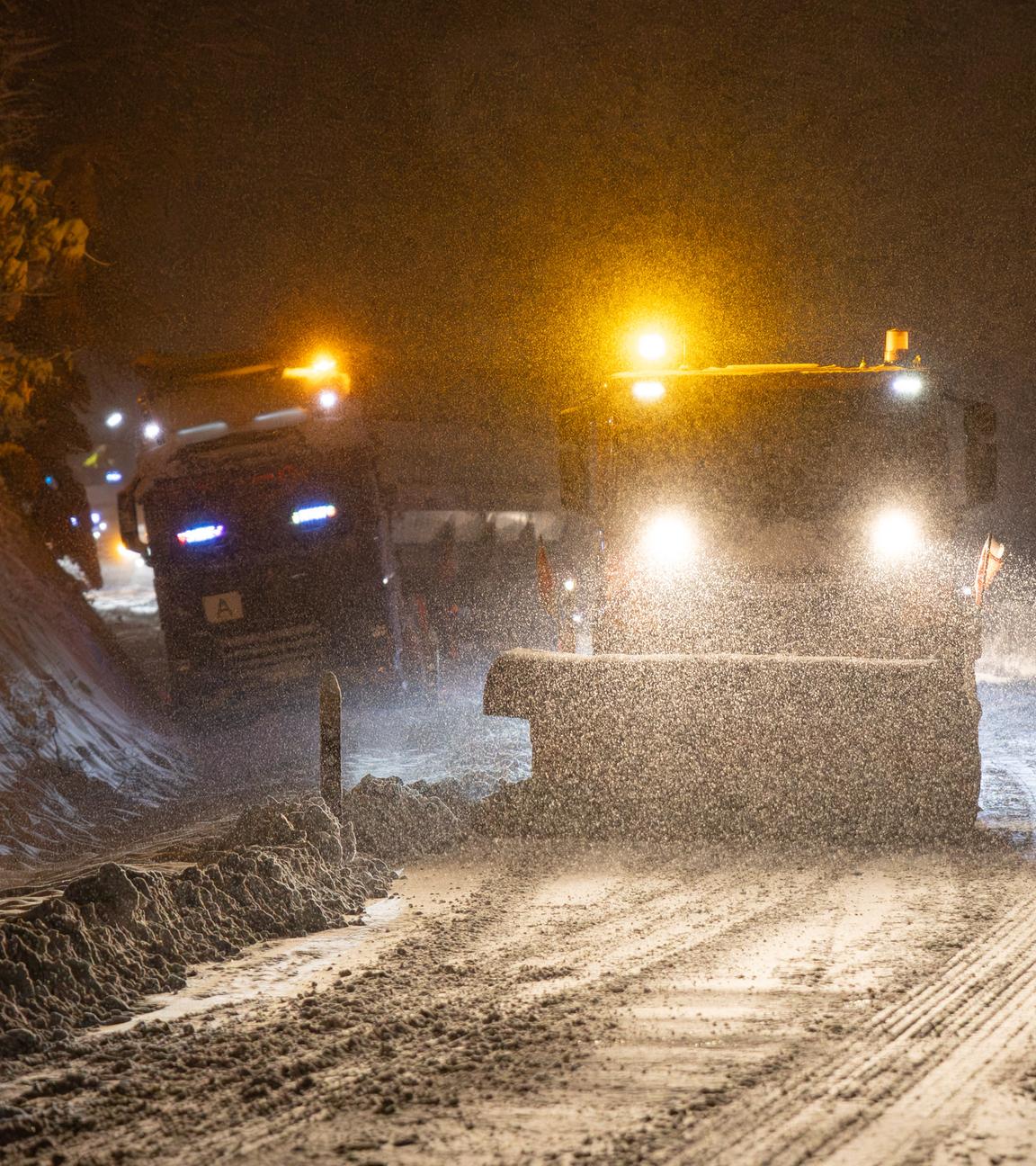 Ein Räumfahrzeug vom Winterdienst befreit bei Dunkelheit eine Landstraße vom Schnee.