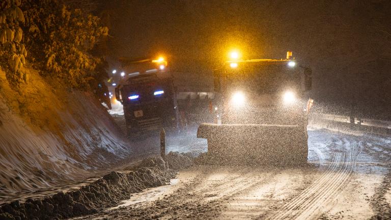 Ein Räumfahrzeug vom Winterdienst befreit bei Dunkelheit eine Landstraße vom Schnee.