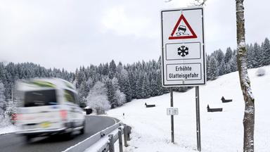 Ein Lieferwagen fährt über eine Straße an einem Schild mit der Aufschrift Erhöhte Glatteisgefahr entlang.