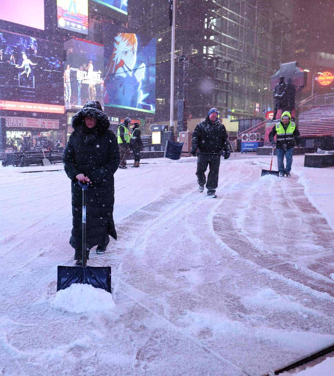 Mehrere Menschen mit Schneeschaufeln räumen Schnee am Times Square in New York.