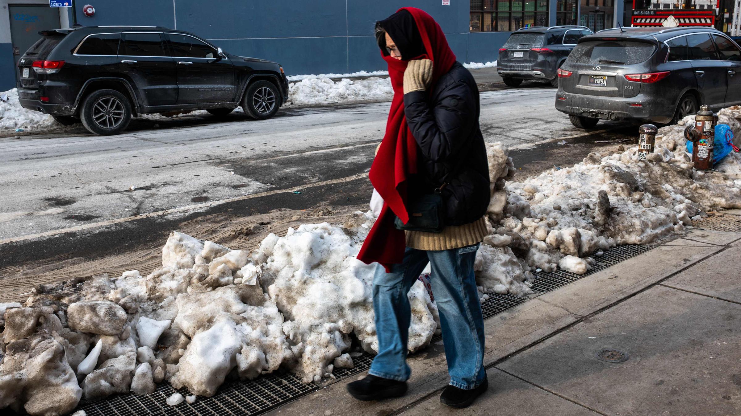 Eine Person in Winterkleidung geht an schmutzigen Schneehaufen in New York vorbei.