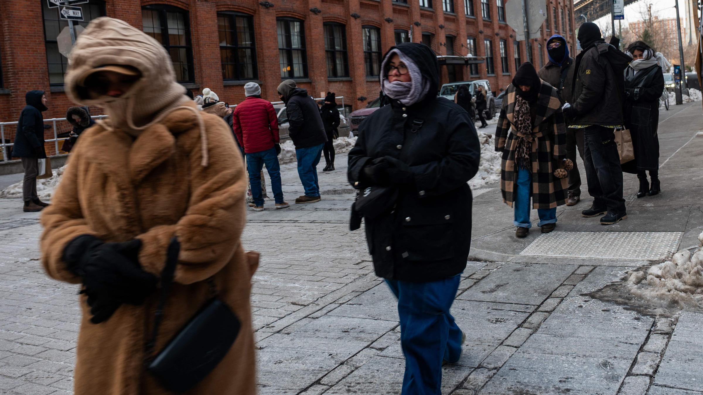 Menschen in dicker Winterkleidung gehen durch eine verschneite Straße im New Yorker Stadtteil Brooklyn.
