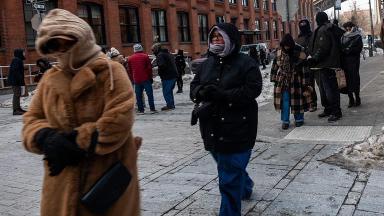Menschen in dicker Winterkleidung gehen durch eine verschneite Straße im New Yorker Stadtteil Brooklyn.