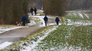 Spaziergänger gehen am Rand der Felder entlang, auf denen der Schnee langsam taut, aufgenommen am 16.02.2025 in Mayen (Eifel)