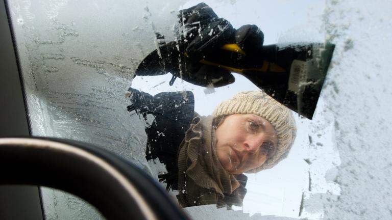 Eine Frau kratzt Schnee und Eis von ihrer Windschutzscheibe weg.
