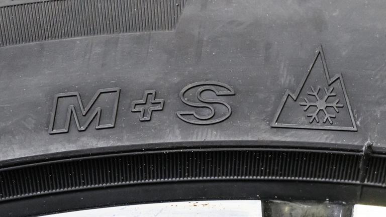 Auf einem schwarzen Autoreifen stehen die Buchstaben M + S. Daneben ist ein Symbol mit einem Berg und einer Schneeflocke.
