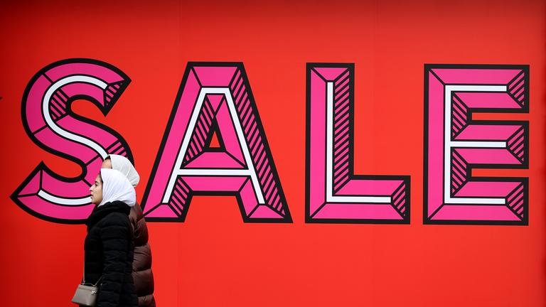 Zwei Frauen laufen an einem großen Schild, welches das Wort SALE zeigt, vorbei.