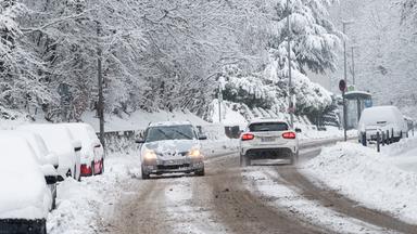 Zwei Autos fahren auf einer verschneiten Straße entlang. 