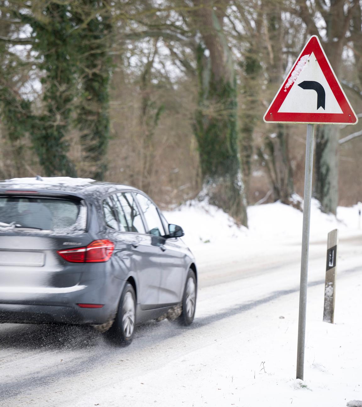 Ein Auto fährt auf einer schneebedeckten Landstraße an einem Verkehrschild vorbei.