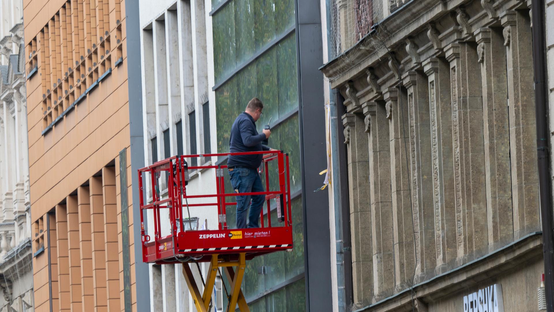Ein Mann auf einer Hebebühne bearbeitet in einer Fußgängerzone eine Fassade. (Symbolbild für die Prognose des IWF)