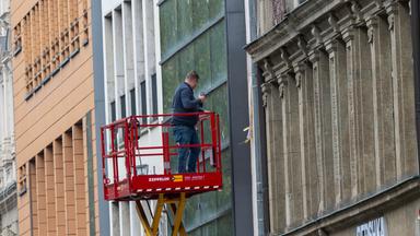 Ein Mann auf einer Hebebühne bearbeitet in einer Fußgängerzone eine Fassade